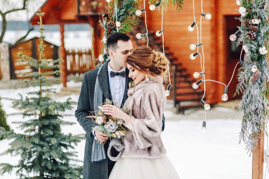 Groom tenderly embracing her beautiful bride. Winter wedding ceremony in rustic style outdoors.
